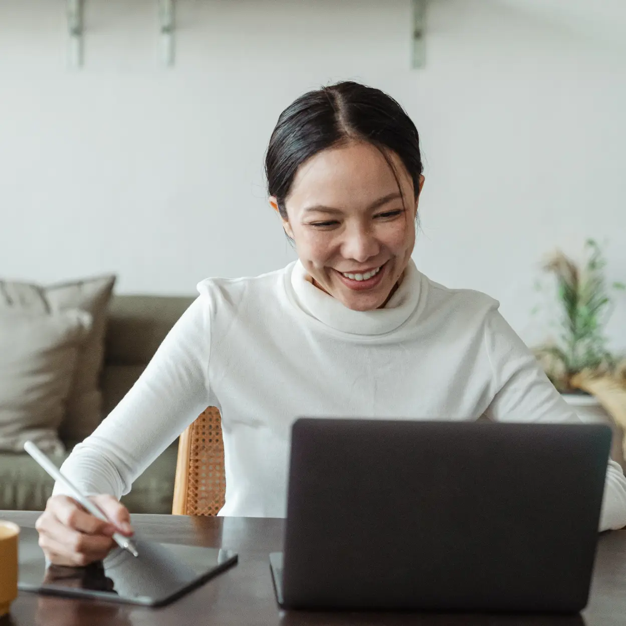 Woman smiling, using laptop and graphic tablet at home.